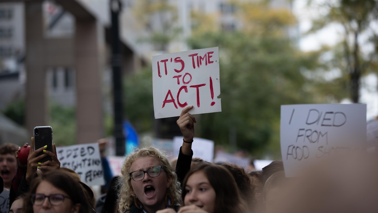 Une adolescente parmi la foule dresse une affiche avec l'inscription « C'est le temps d'agir ».