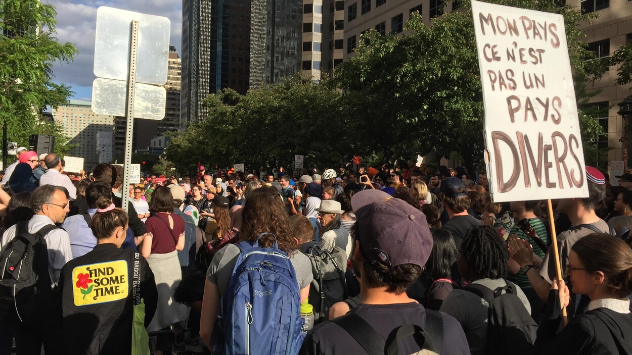 Une foule rassemblée sur la rue à Montréal; l'une des personnes porte une pancarte où l'on peut lire : « Mon pays, ce n'est pas un pays divers ».