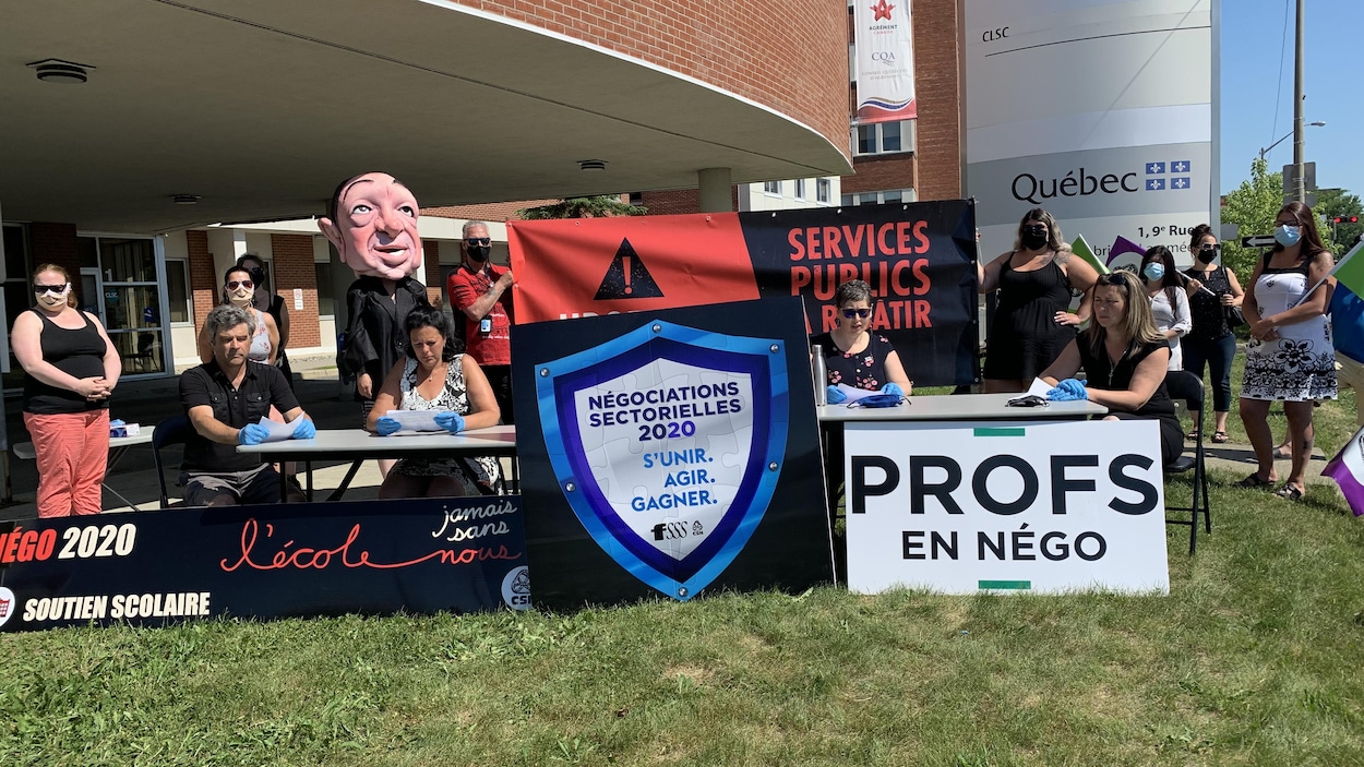 Quatre personnes sont assises à une table à l'extérieur avec des affiches et des pancartes.