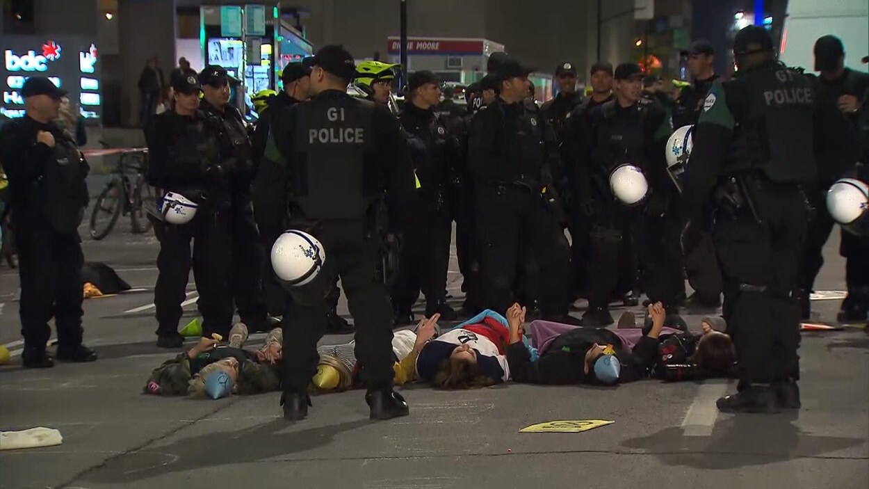 Des manifestants sont couchés au sol et entourés de policiers.