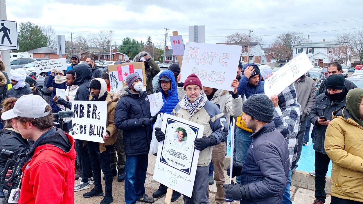 Des gens rassemblés à l'extérieur brandissent des pancartes.