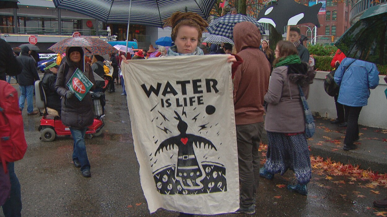 Une femme tend une bannière « Water is life » lors d'une manifestation.