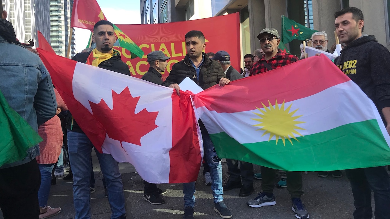 Des hommes présentent les drapeaux canadien et kurde.