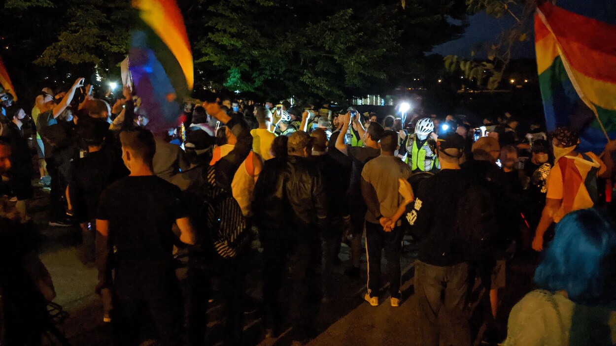 Une foule de manifestants agitant des drapeaux de la Fierté entoure des policiers et le groupe de David Lynn.