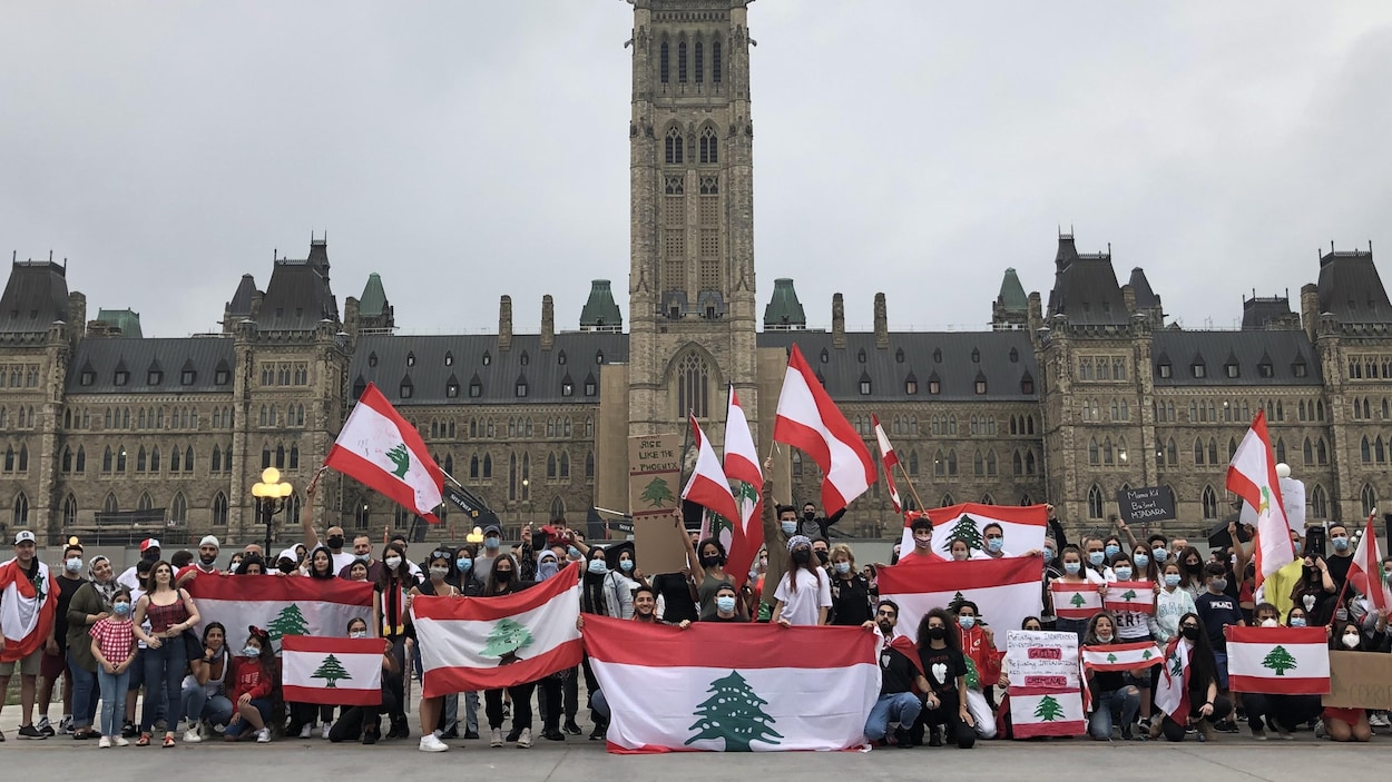 Des dizaines de personnes portant des masques posent avec des drapeaux du Liban devant le parlement d'Ottawa.