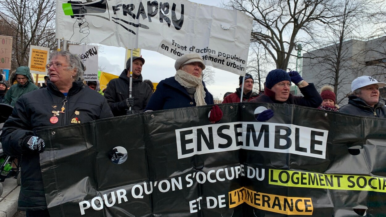 Une dizaine de personnes tiennent des banderoles. Sur l'une d'elle, on peut lire : « Ensemble, pour qu'on s'occupe du logement social et de l'itinérance ».