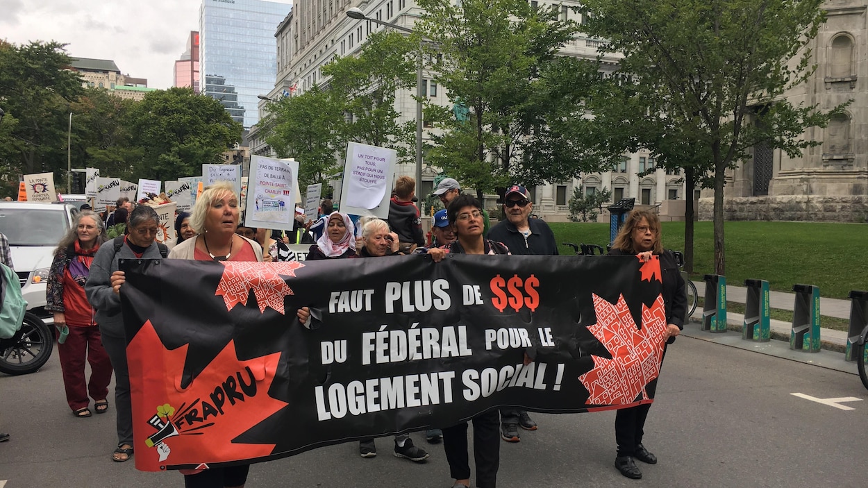 Des manifestants tiennent une banderole sur laquelle on peut lire «Faut plus de dollars du fédéral pour le logement social».