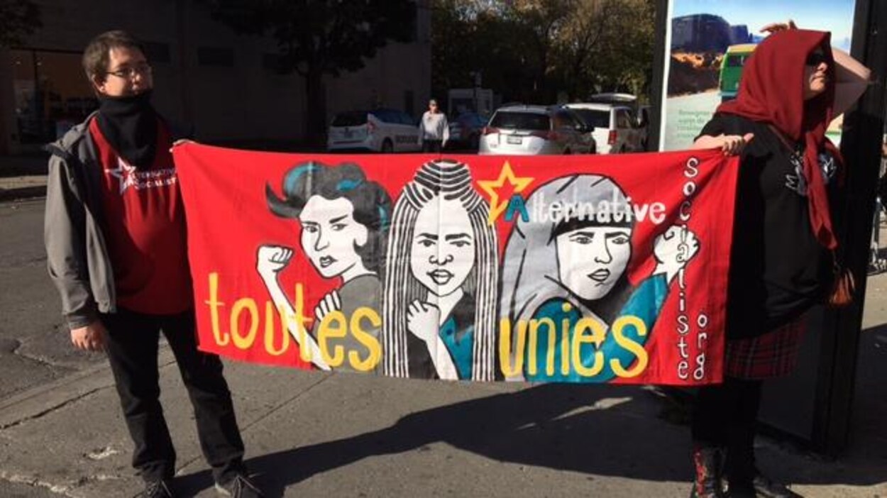 Des manifestants tiennent une banderole affichant le slogan « Toutes unies ». Des manifestants tiennent une banderole affichant le slogan « Toutes unies ».