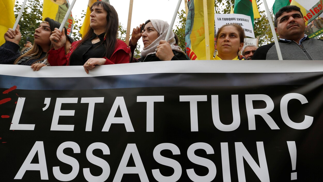 Des manifestants tiennent des pancartes et une large banderole où on peut lire : L'État turc assassin!