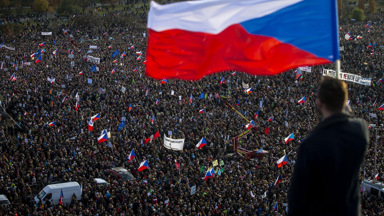 Un homme de dos tient un drapeau tchèque devant une foule de plusieurs dizaines de milliers de manifestants, à Prague, le 16 novembre 2019.