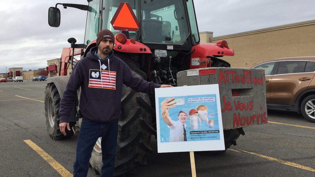 Un producteur de lait devant son tracteur avec une pancarte où on voit Justin Trudeau. Un producteur de lait devant son tracteur avec une pancarte où on voit Justin Trudeau.