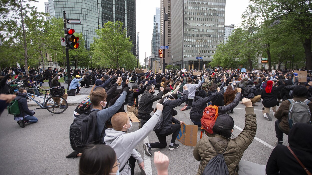 Des manifestants mettent un genou au sol et lèvent le poing à la place du Canada au centre-ville de Montréal.