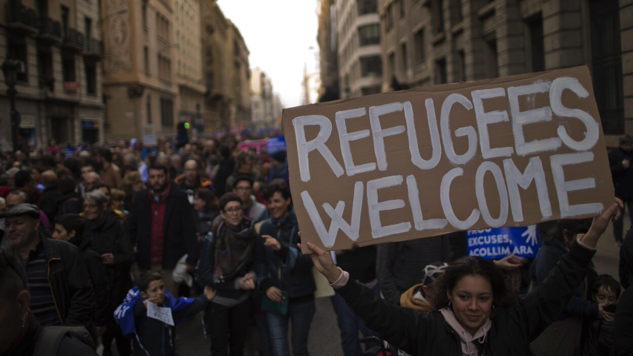 Une manifestante qui tient une pancarte disant « Bienvenue aux réfugiés » marche parmi des milliers de protestataires à Barcelone, en Espagne.