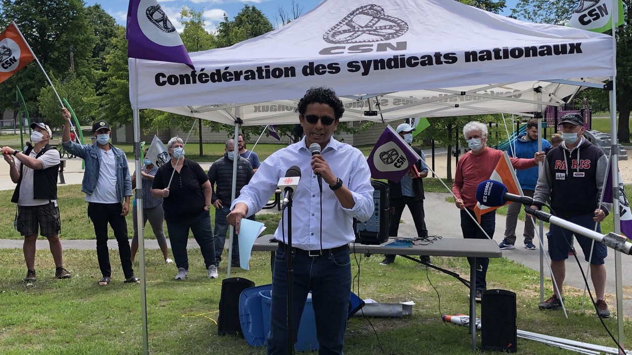 Alfonso Ibarra Ramirez parle au micro. Derrière lui, des travailleurs manifestent tout en portant un masque.