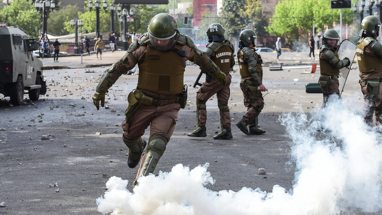 Un gaz lacrymogène au sol à côté de policiers antiémeute.