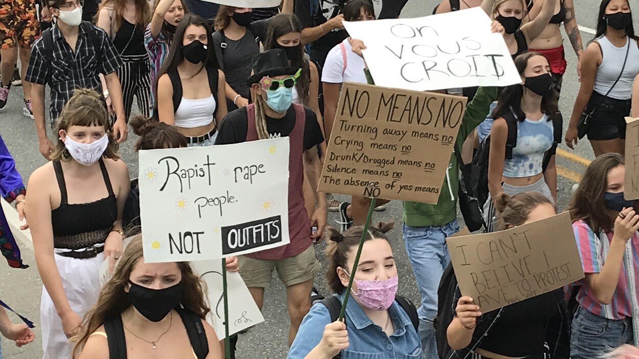 Des hommes et des femmes portant un masque marchent avec des pancartes dans les mains.