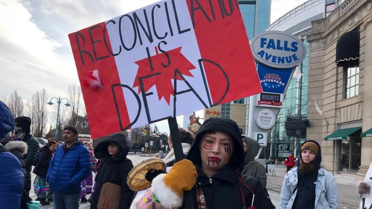 Une manifestante avec une pancarte sur laquelle est inscrit « la réconciliation est morte ».