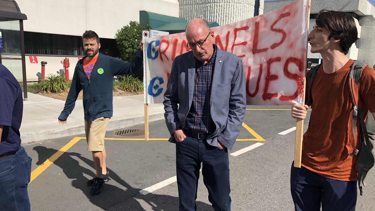 Yves Lévesque suivi de deux manifestants tenant une bannière.