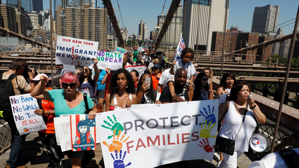 Des manifestantes tiennent une grande banderole indiquant en anglais: " protégez les familles". La marche a lieu sur le pont de Brooklyn.