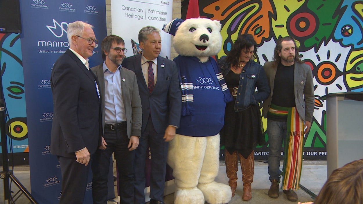 De gauche à droite : Stuart Murray, coprésident de Manitoba 150, Steven Guilbeault, ministre fédéral du Patrimoine, Dan Vandal, député fédéral de Saint-Boniface et Saint-Vital et ministre des Affaires du Nord, une mascotte déguisée en ours à l'effigie de Manitoba 150 et deux artistes franco-manitobains.