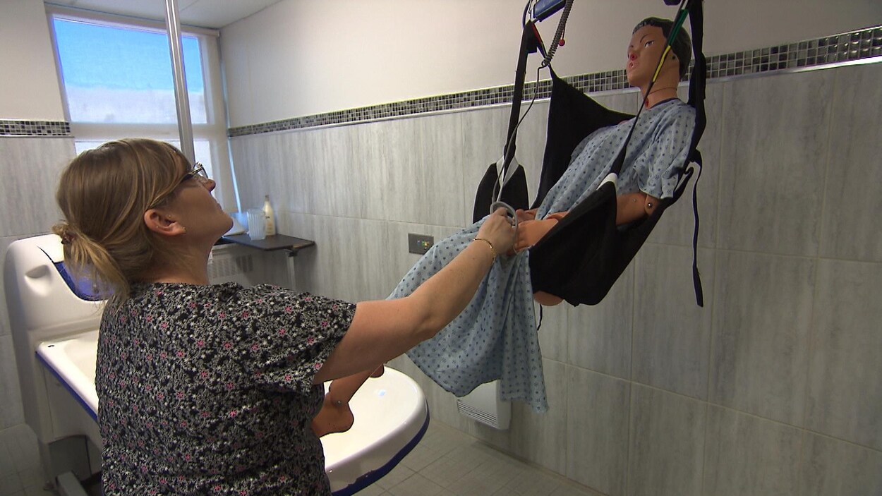 Une préposée transporte un mannequin avec un lève-personne.
