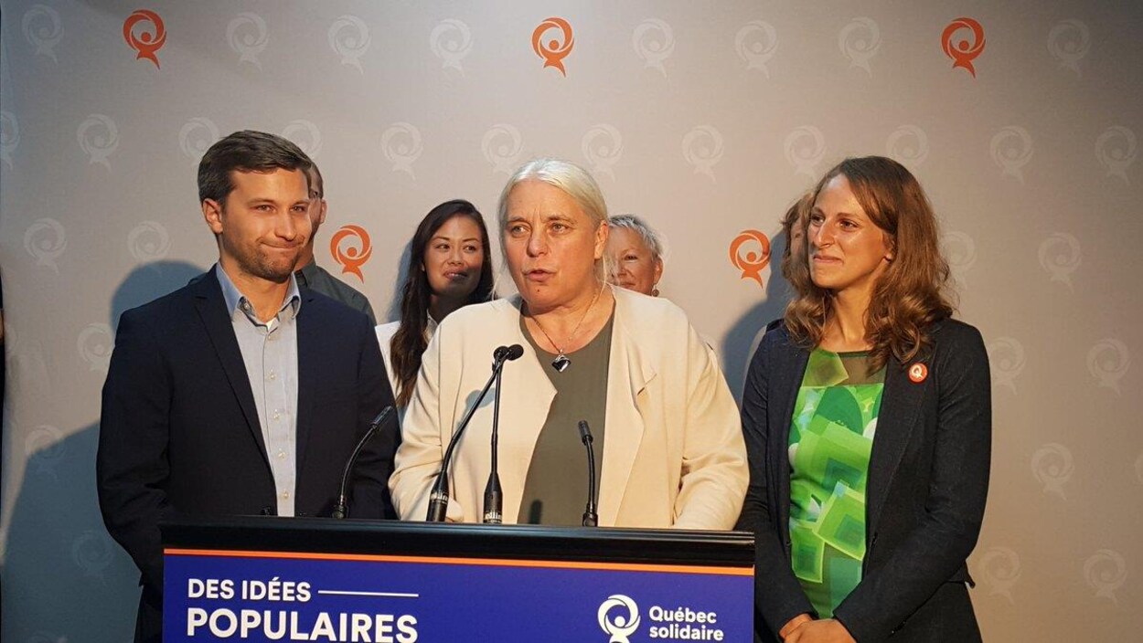 Manon Massé entourée de membres de son équipe parle dans un micro.