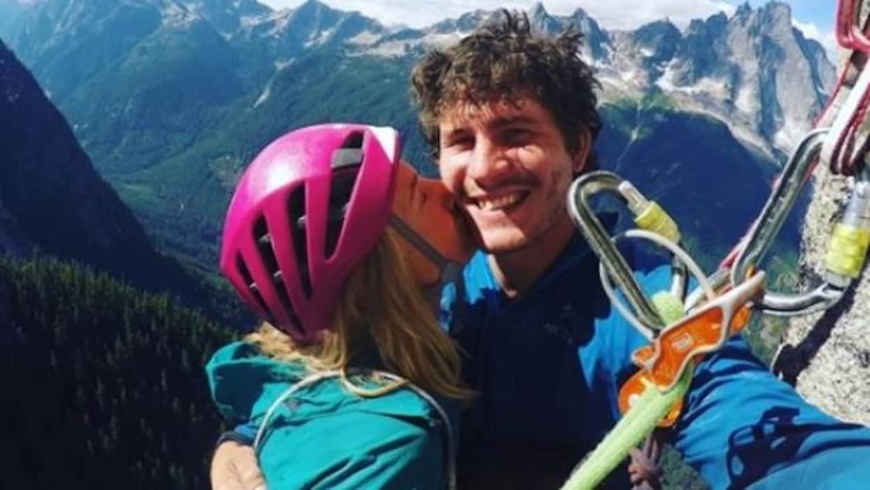 Une jeune femme blonde embrasse un jeune homme aux cheveux bruns frisés sur la joue. Ils sont au sommet d'une montagne. Une jeune femme blonde embrasse un jeune homme aux cheveux bruns frisés sur la joue. Ils sont au sommet d'une montagne.