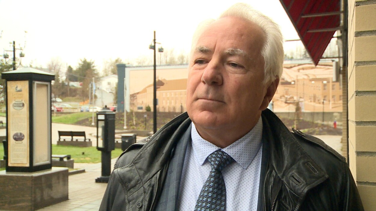 Portrait de Marcel Furlong en complet cravate sous un manteau de cuir, à l'extérieur lors d'une journée grise.