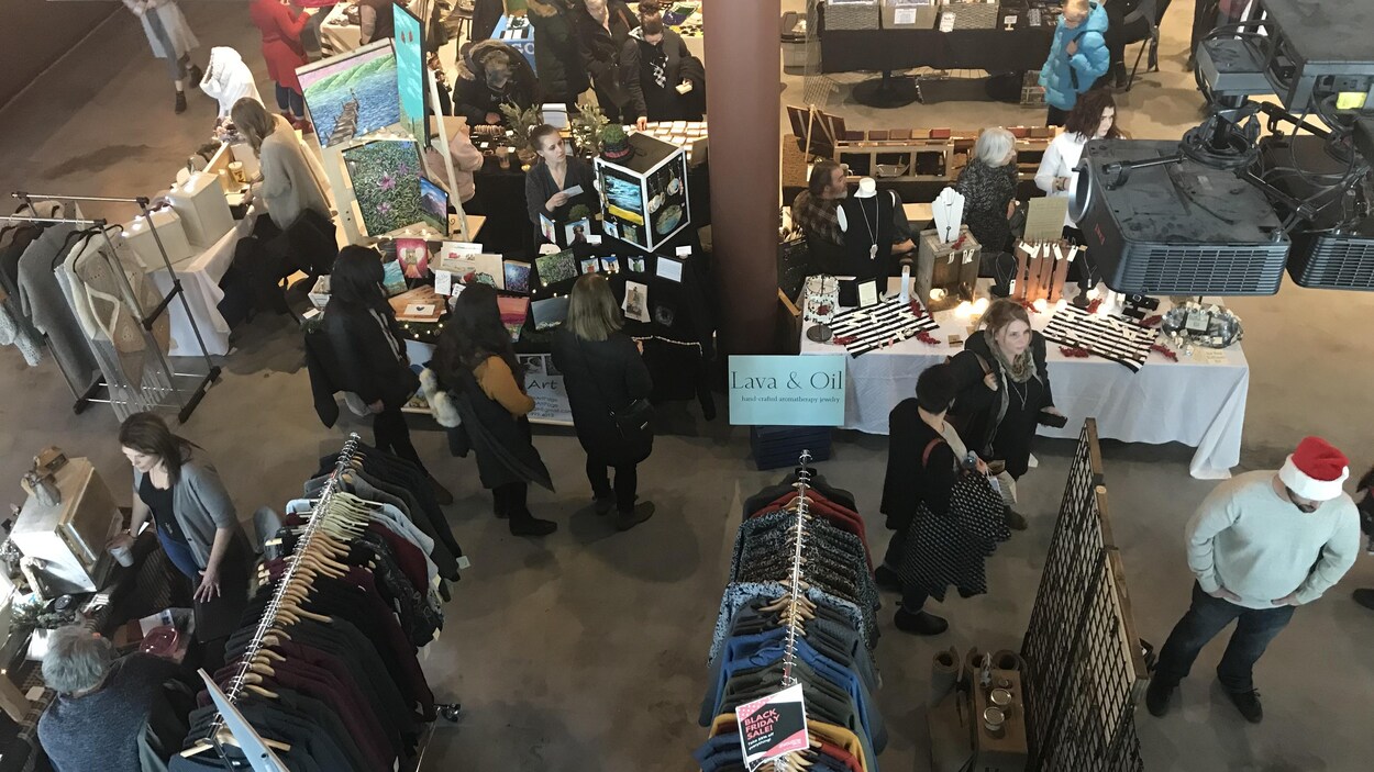 Une vue de haut du marché artisanal de Noël avec des habits en vente et des clients circulant dans les allées.