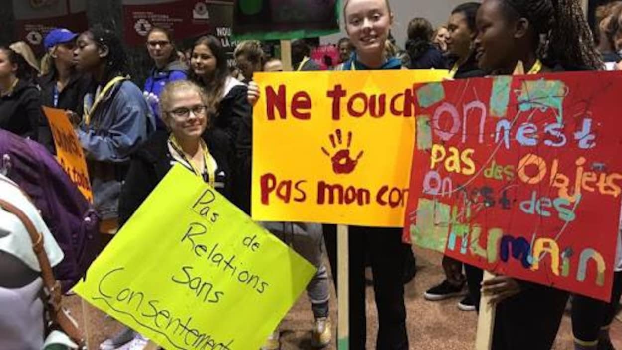 Trois jeunes femmes dans une foule tenant des pancartes faisant la promotion des relations sexuelles consensuelles.