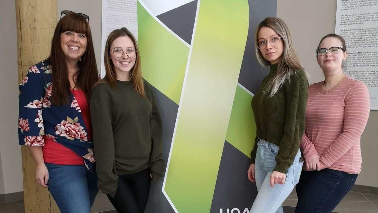 Quatre jeunes femmes posent de chaque côté d'une affiche avec un ruban vert symbolisant la persévérance scolaire.