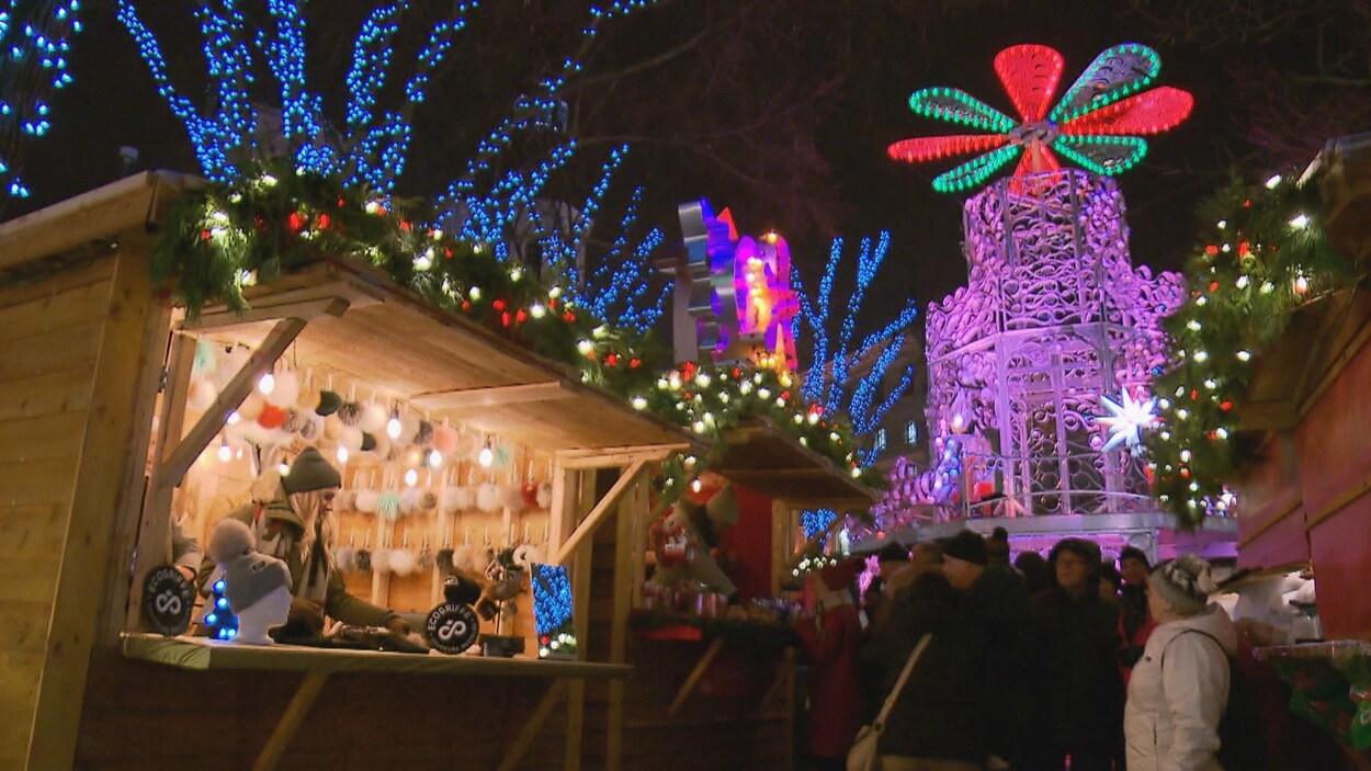 Des passants déambulent devant des kiosques de bois illuminés pour le marché de Noël Allemand Des passants déambulent devant des kiosques de bois illuminés pour le marché de Noël Allemand