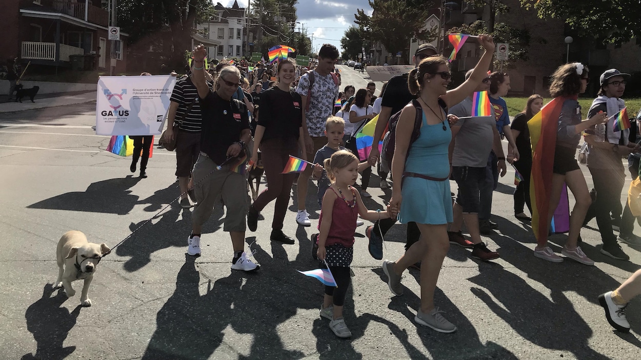Une foule déambule avec des drapeaux arc-en-ciel.