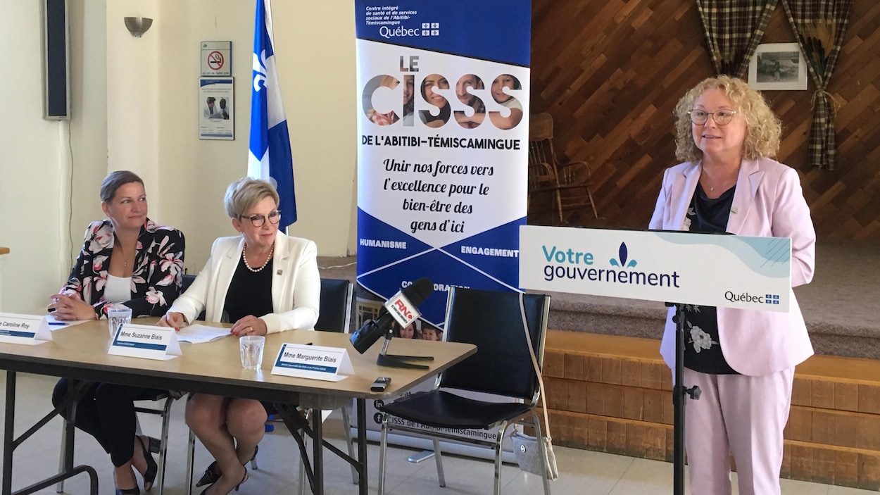 Marguerite Blais parle derrière un lutrin du gouvernement du Québec, la députée Suzanne Blais et la PDG du CISSS-AT Caroline Roy derrière elle.