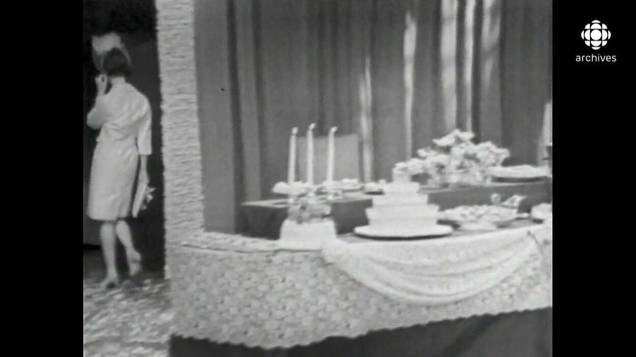 Une femme de dos, quitte une salle décorée pour un mariage avec gâteau, arrangement floral et chandelier.