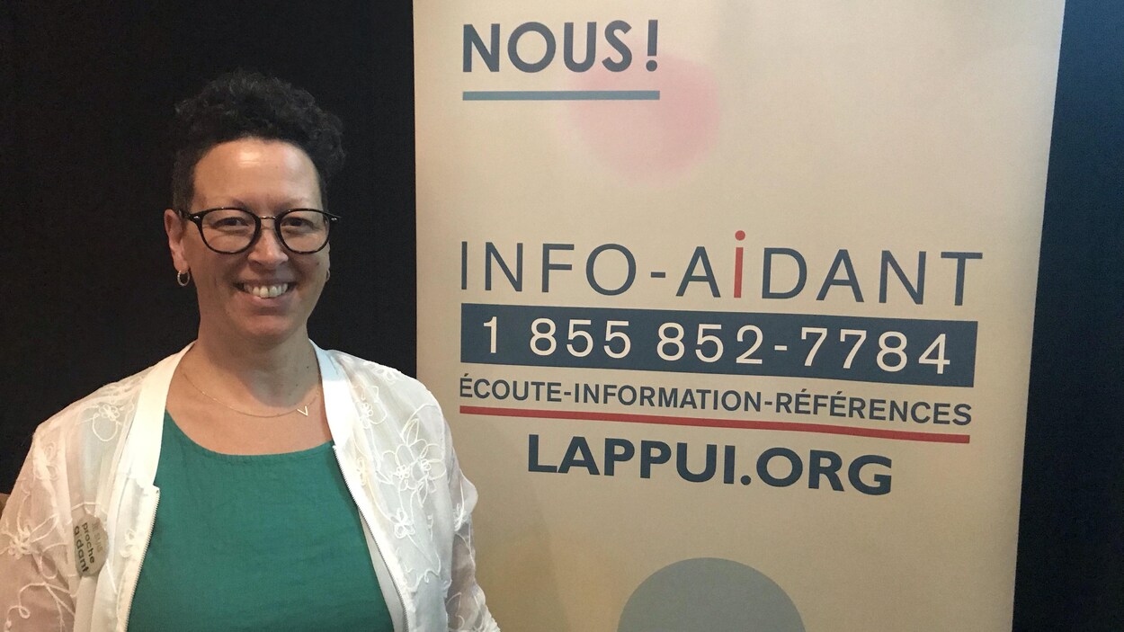 Une femme pose devant une affiche d'Info-Aidant, une ligne téléphonique.
