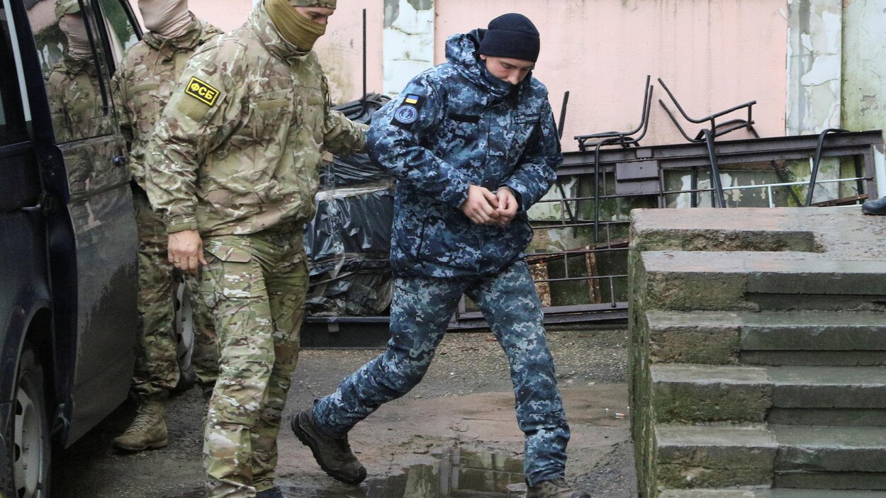 Un policier escorte un soldat menotté.