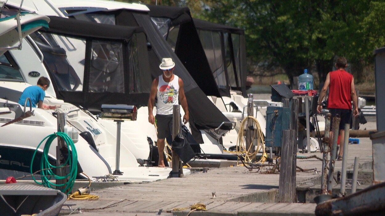 Des hommes se promènent sur un quai auquel sont amarrés plusieurs bateaux.