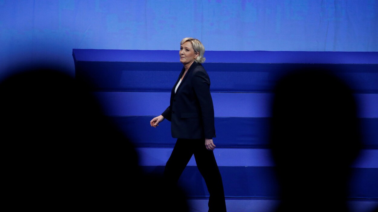 Marine Le Pen, habillé en complet noir, marche sur une scène. Marine Le Pen, habillé en complet noir, marche sur une scène.