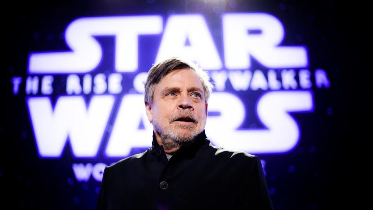 Portrait de Mark Hamill avec, en toile de fond, un mur portant l'inscription Star Wars.