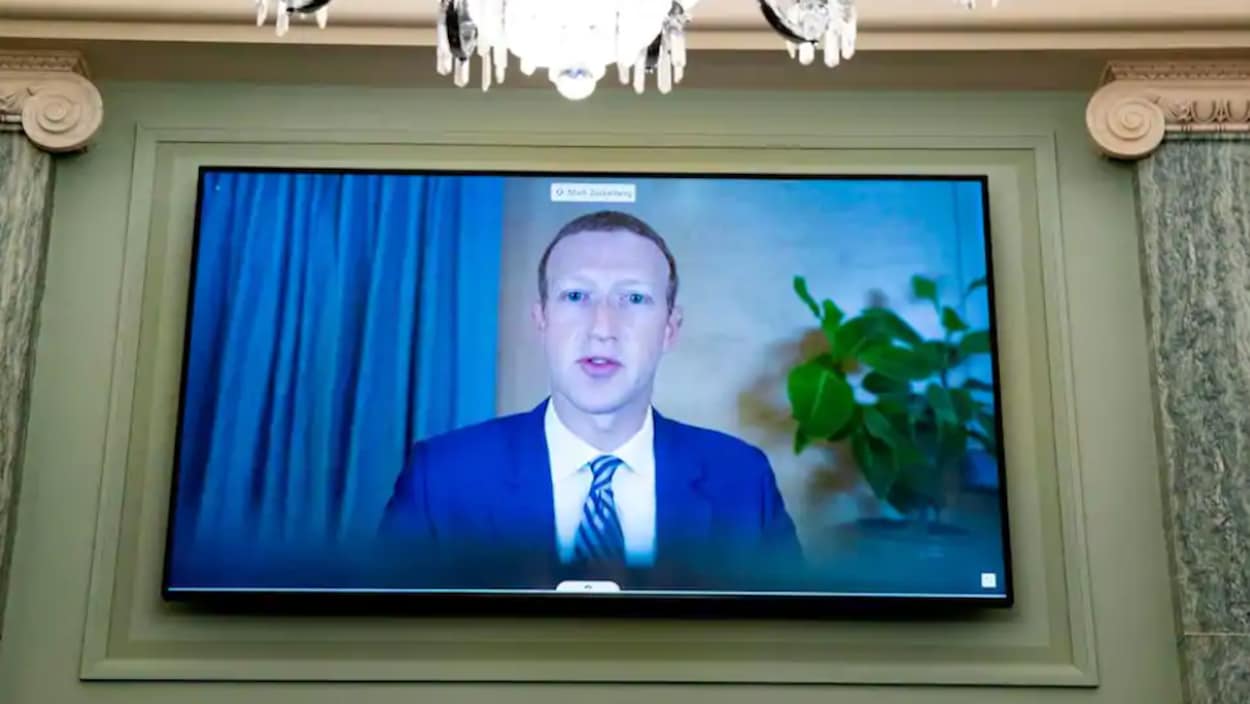 L'image de Mark Zuckerberg en train de parler est projetée sur une télévision à écran plat dans une pièce luxueuse.