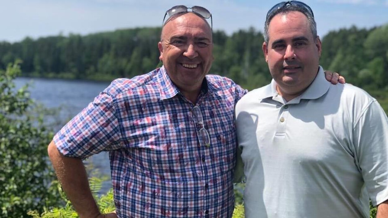 Bernard Généreux et Martin Ferron posent bras dessus, bras dessous devant un lac.