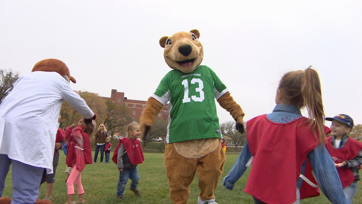 La mascotte de l'équipe des Riders, une personne avec un costume d'écureuil en peluche portant un maillot vert, joue avec des enfants sur un gazon.