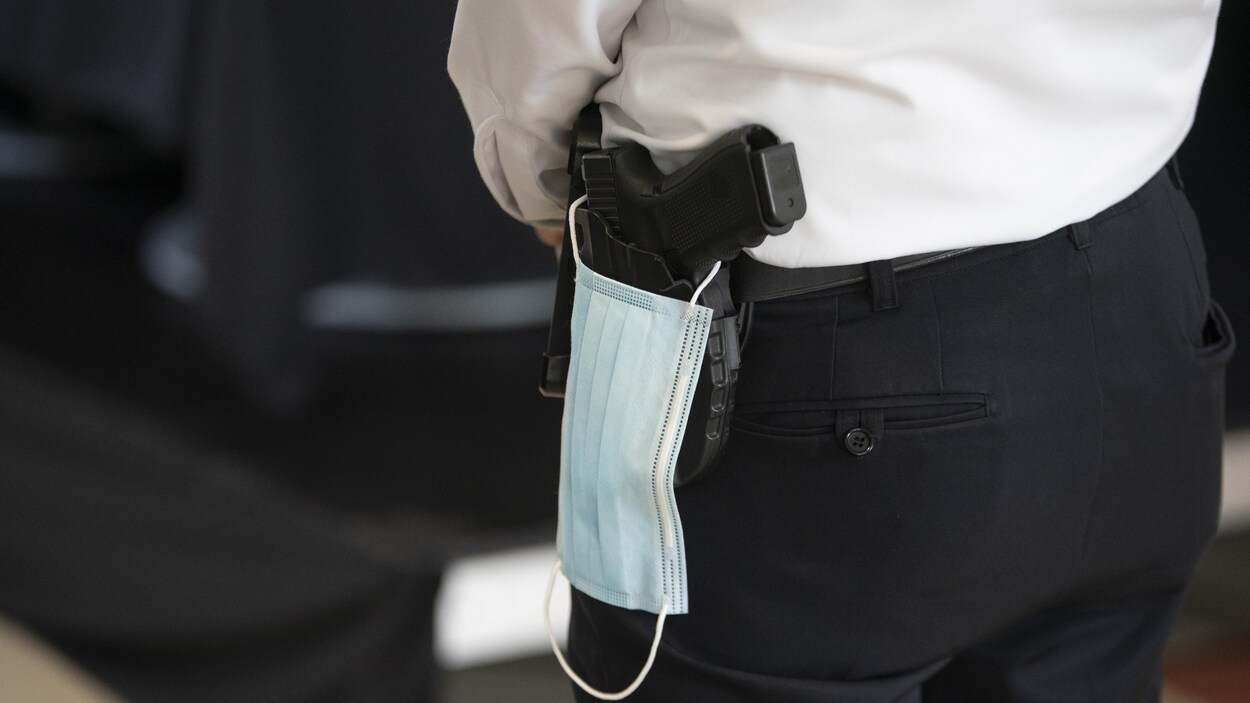 Un masque accroché sur l'arme de service que porte un policier en uniforme.