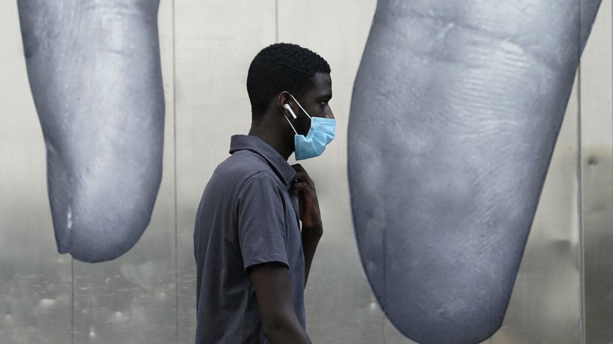 Un homme portant un masque passant devant une murale à New York.