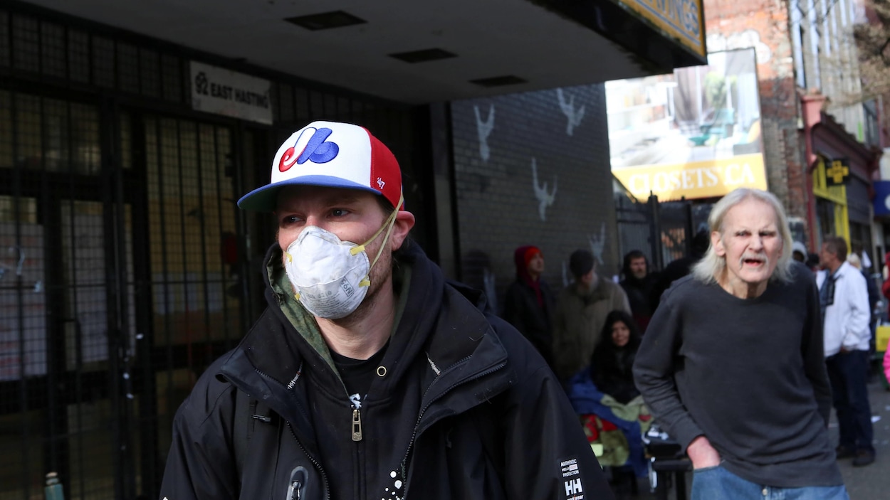 Un homme coiffé d'une casquette des Expos marche dans la rue avec un masque N95 pour se protéger du coronavirus.