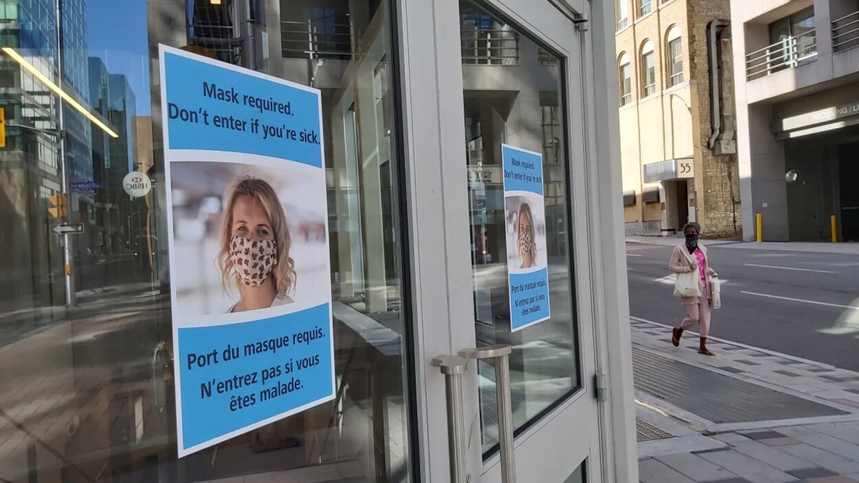 Une affiche sur la porte extérieure d'un immeuble donnant accès au train léger rappelle que le porte du masque est requis.