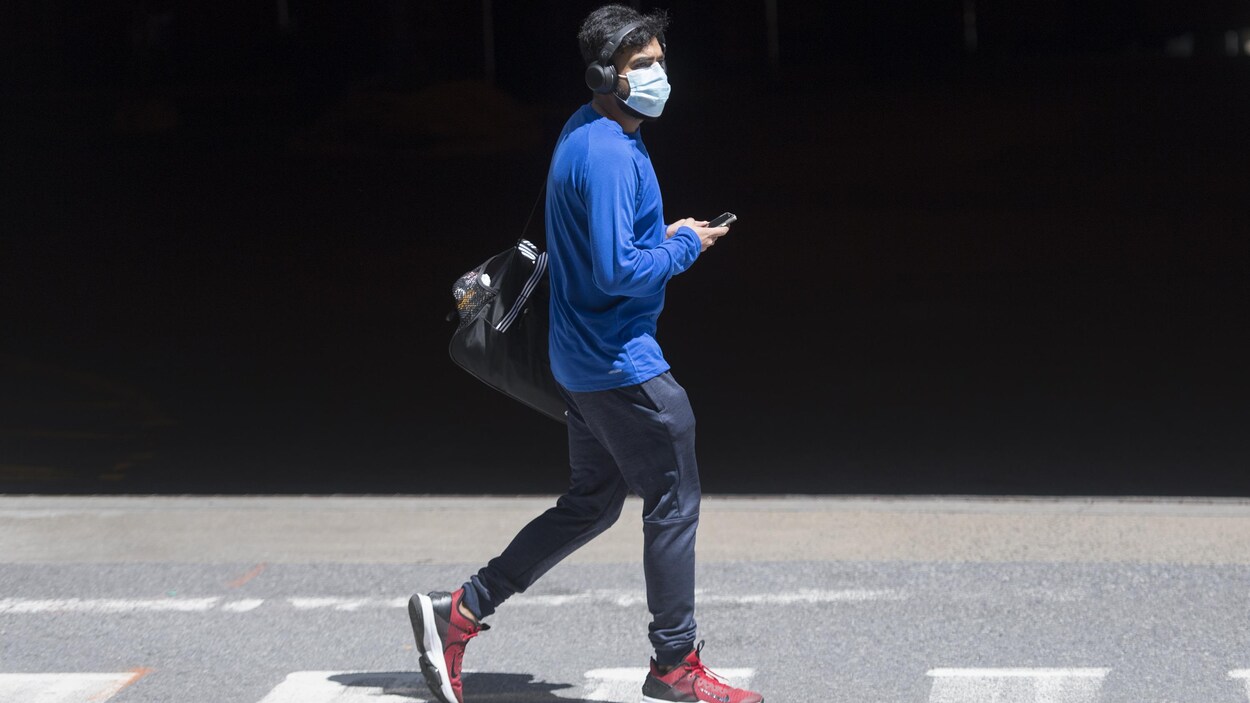 Un homme portant un masque et des écouteurs marche sur un passage piéton.