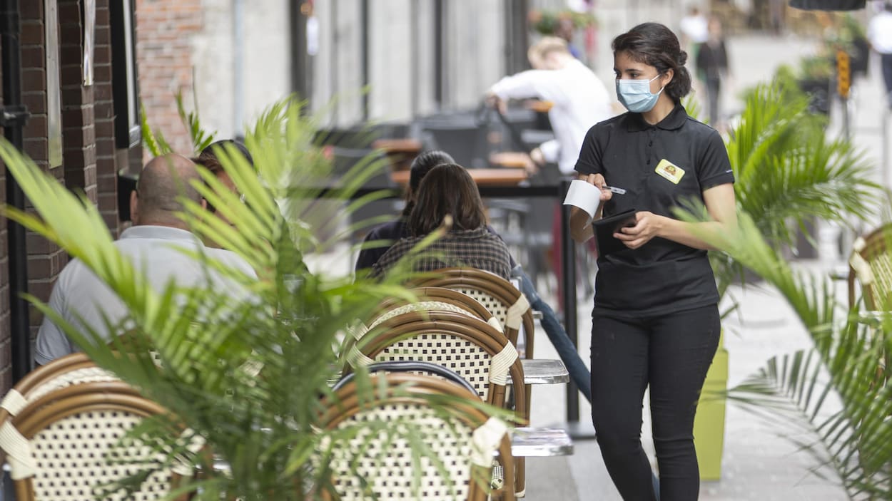 Quelques clients assis à une terrasse d'un restaurant et une serveuse portant un masque.