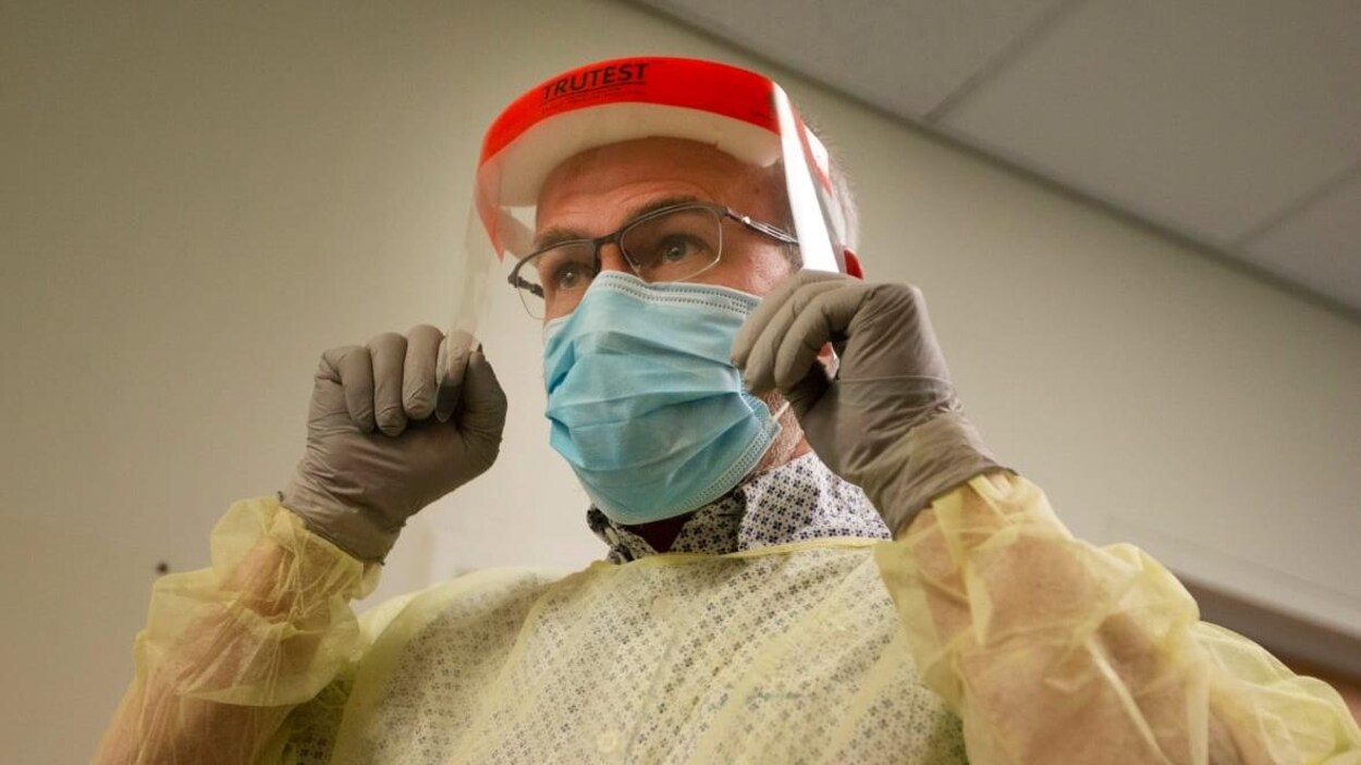 Un médecin porte l'équipement de protection individuelle : un masque, une blouse, des gants et une visière.